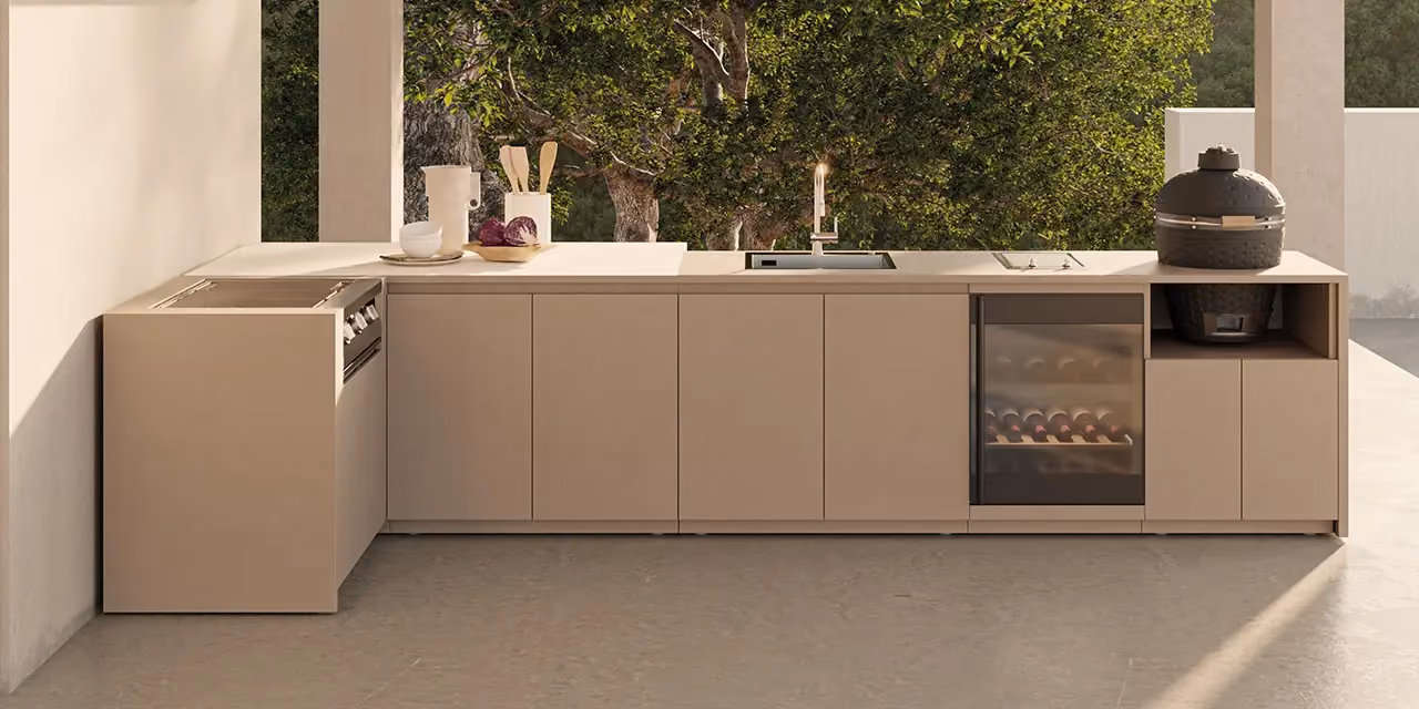Lange taupefarbene Außenküche unter einem Portikus, mit Spüle, verglastem Weinkühlschrank und schwarzem Kamado-Grill, vor einem Baum