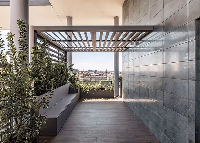 Panoramic terrace under a dark pergola, with an integrated planter-seat and a view over the city rooftops.
