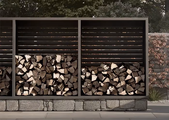 Moderner Außen-Holzunterstand aus dunklem Metall mit waagerecht gelatteten oberen Paneelen und mit Brennholz gefüllten unteren Fächern, vor einer niedrigen Natursteinmauer.