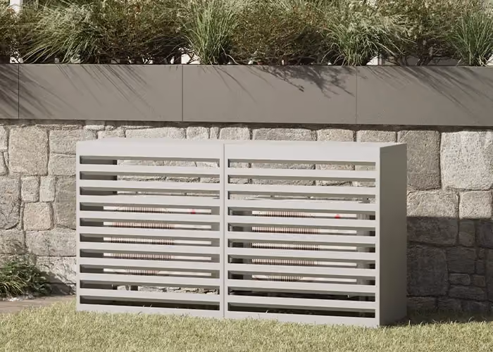Moderne Abdeckung für ein Außengerät mit hellgrauem, waagerecht gelattetem Metallrahmen, in einem Garten vor einer Natursteinwand und einem bepflanzten Gefäß.