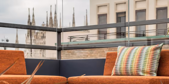 Fioriere scure con pannello in vetro trasparente delimitano un terrazzo con divano arancione