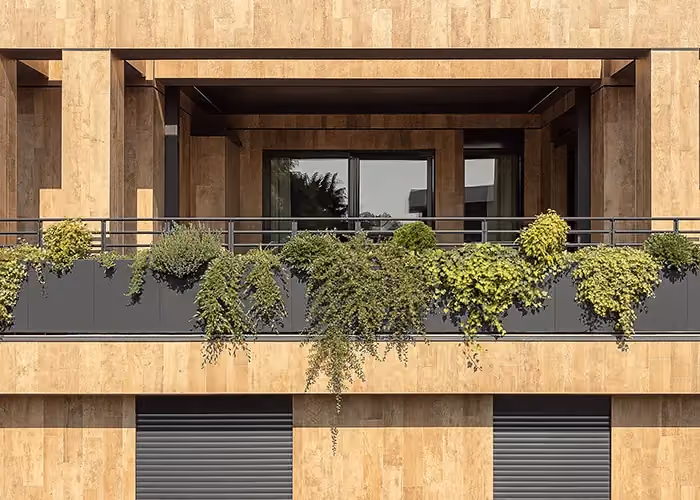 Balcone moderno con lunga fioriera parapetto in metallo scuro e piante ricadenti verdi applicata alla ringhiera dell’edificio.