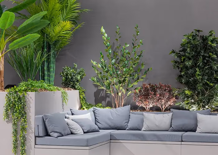 Modulares Außensofa mit grauen Kissen und großen integrierten Pflanzgefäßen mit grünen Zierpflanzen, auf minimalistisch dunklem Grund.