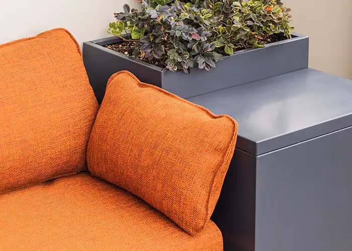 Detail eines modularen Außensofas mit orangefarbenen Kissen, dunkelgrauem Metallkorpus und integriertem Pflanzgefäß.