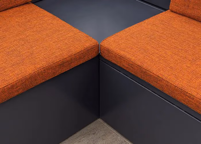 Nahaufnahme modularer Außensitzmöbel mit orangefarbenen Kissen und geometrischem Rahmen aus dunklem Metall.