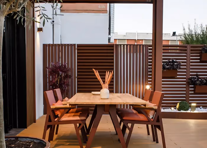 Table à manger et chaises en bois sur un patio extérieur, délimité par des panneaux brise-vue assortis.