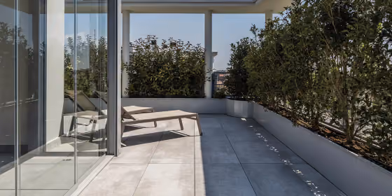 Pavimentazione sopraelevata grigia su un terrazzo lungo, delimitato da una vetrata continua