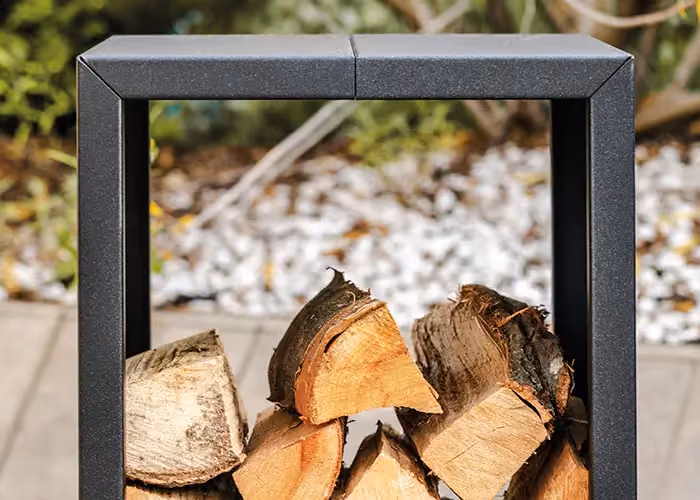 Modern log store with a cubic black metal frame and logs stacked at its centre, set in an outdoor garden.