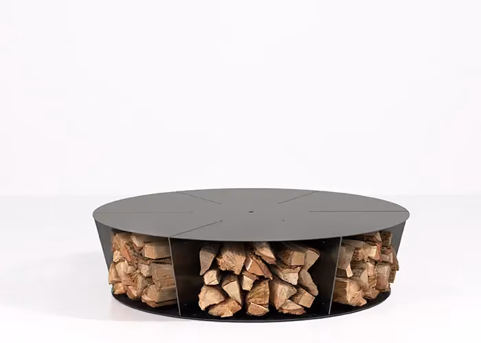 Modern round outdoor fire pit with a black metal frame and open side bays holding firewood, photographed on a minimal white ground.