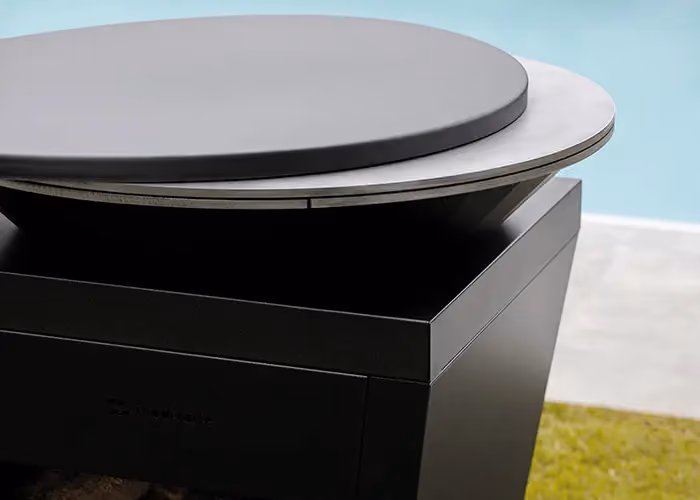 Dettaglio del piano circolare di un barbecue moderno da esterno in metallo nero con superficie di cottura rialzata.