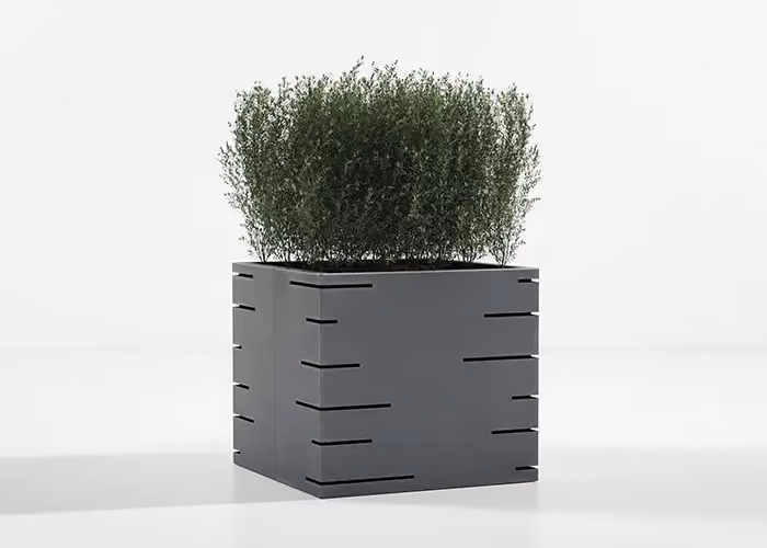 Modern square planter in grey metal with decorative horizontal grooves and a green ornamental shrub, photographed on a minimal white ground.