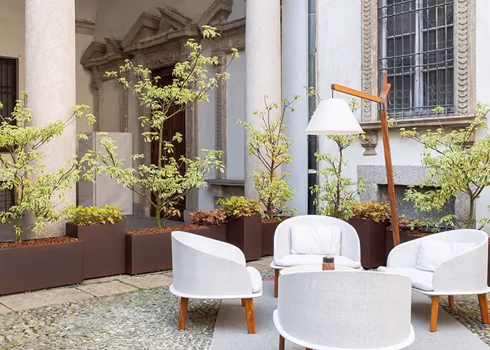 Elegant courtyard with white outdoor seating and large modular planters holding trees and decorative plants, in front of a historic building.