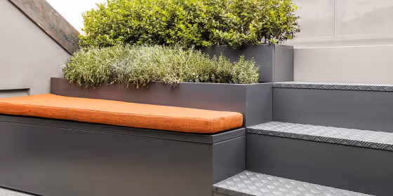 Stepped grey planter with an integrated orange upholstered seat, planted along the high side