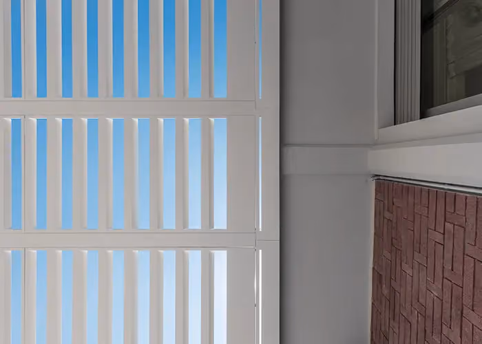 View from below of the sun louvres of a white pergola against a building wall.