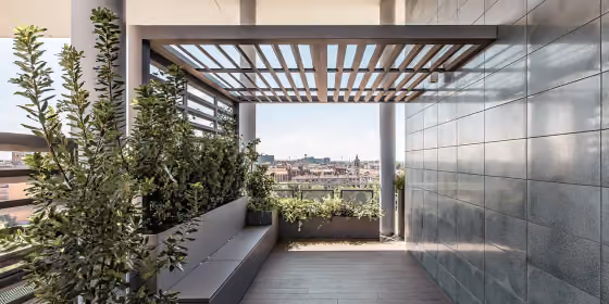 Pergola a lame orientabili su un terrazzo, con fioriere alte e vetrata continua