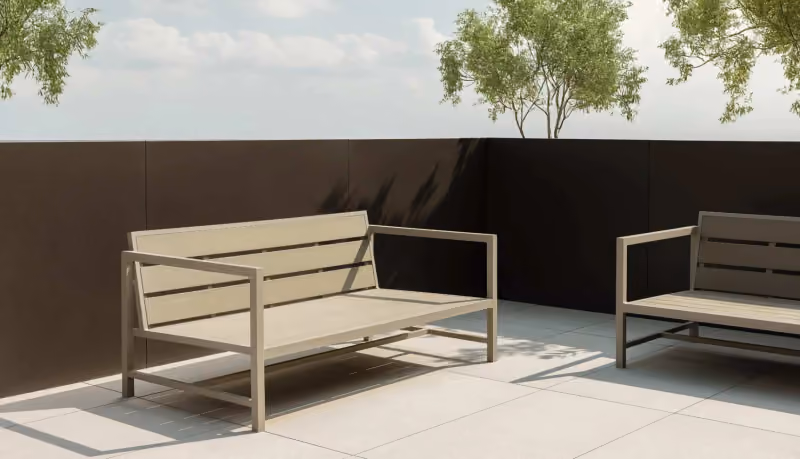 Two modern outdoor armchairs with pale beige seats and a minimal metal frame, on a tiled terrace in front of a dark wall, with trees and daylight behind.
