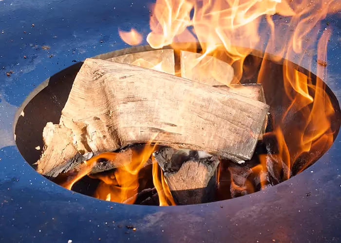 Nahaufnahme eines mit offener Flamme brennenden Scheits in der mittigen Öffnung der Feuerschale.