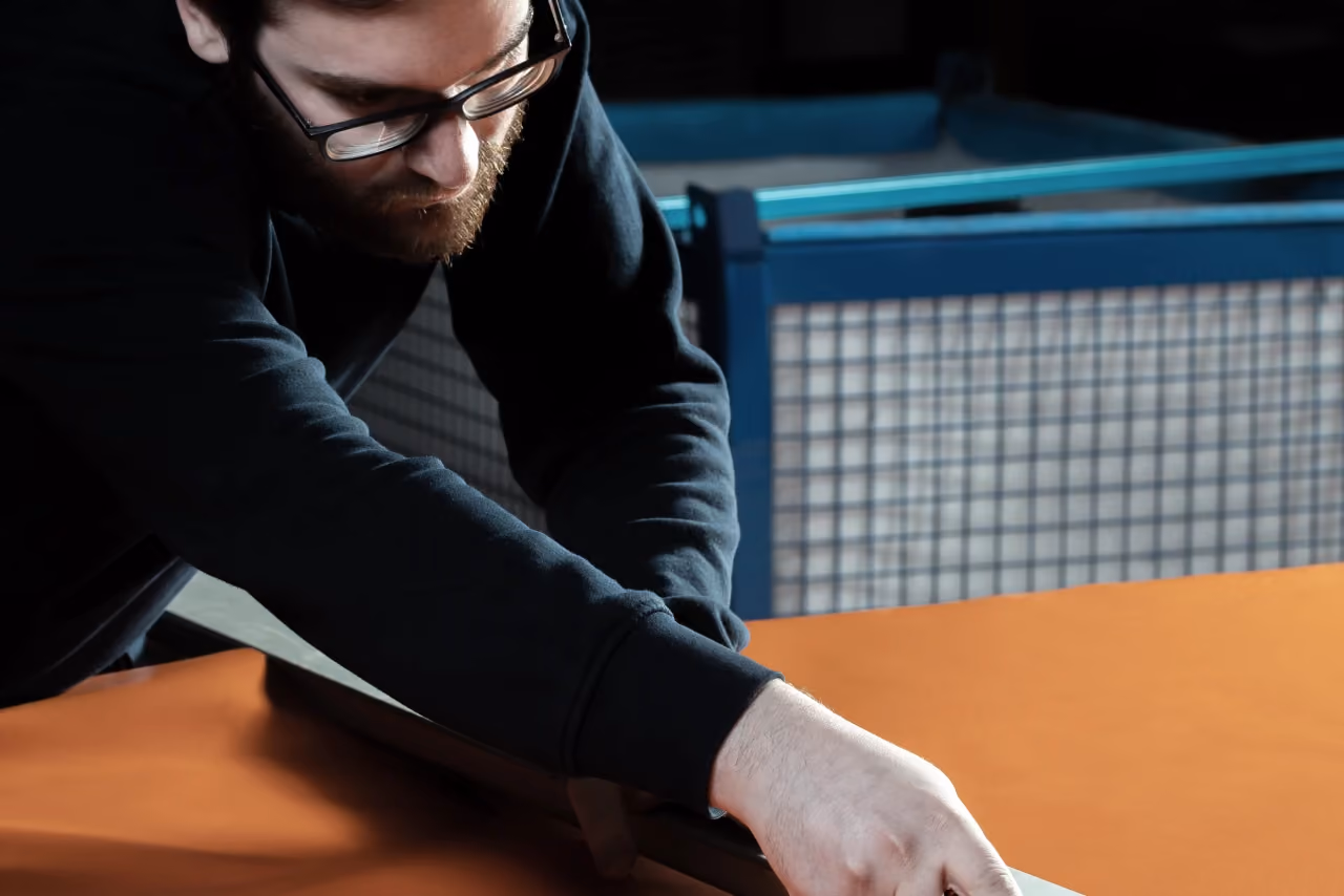 A craftsman in glasses at the workbench, bent over a metal component