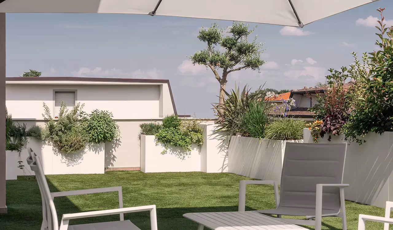 Terrace garden with a green lawn, grey outdoor armchairs under a parasol and white modular corner planters full of plants and small trees.