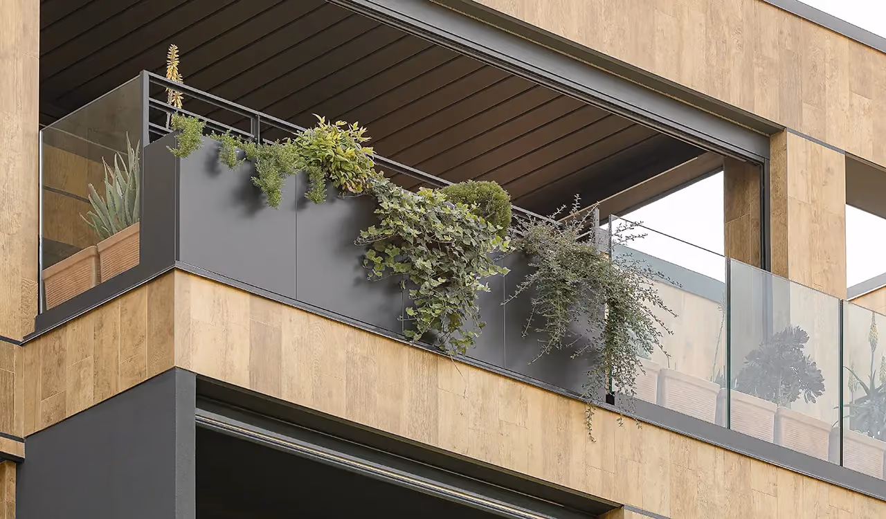 Nahaufnahme eines modernen Balkons mit in die Brüstung integrierten dunkelgrauen Pflanzgefäßen, Kletterpflanzen und einem klaren Glasfeld.