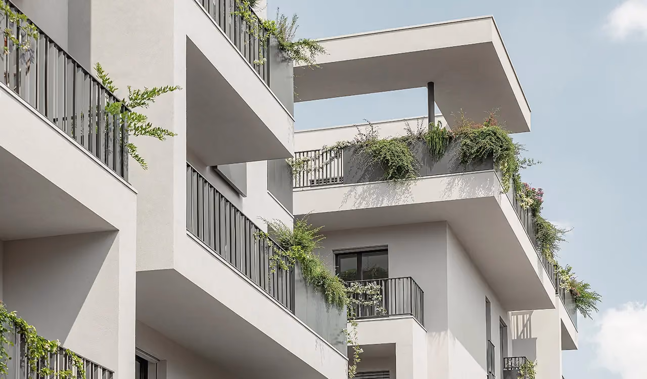 Vue en contre-plongée de balcons et terrasses d'angle modernes sur un bâtiment blanc, avec bacs périmétraux gris d'où retombent des plantes vertes.