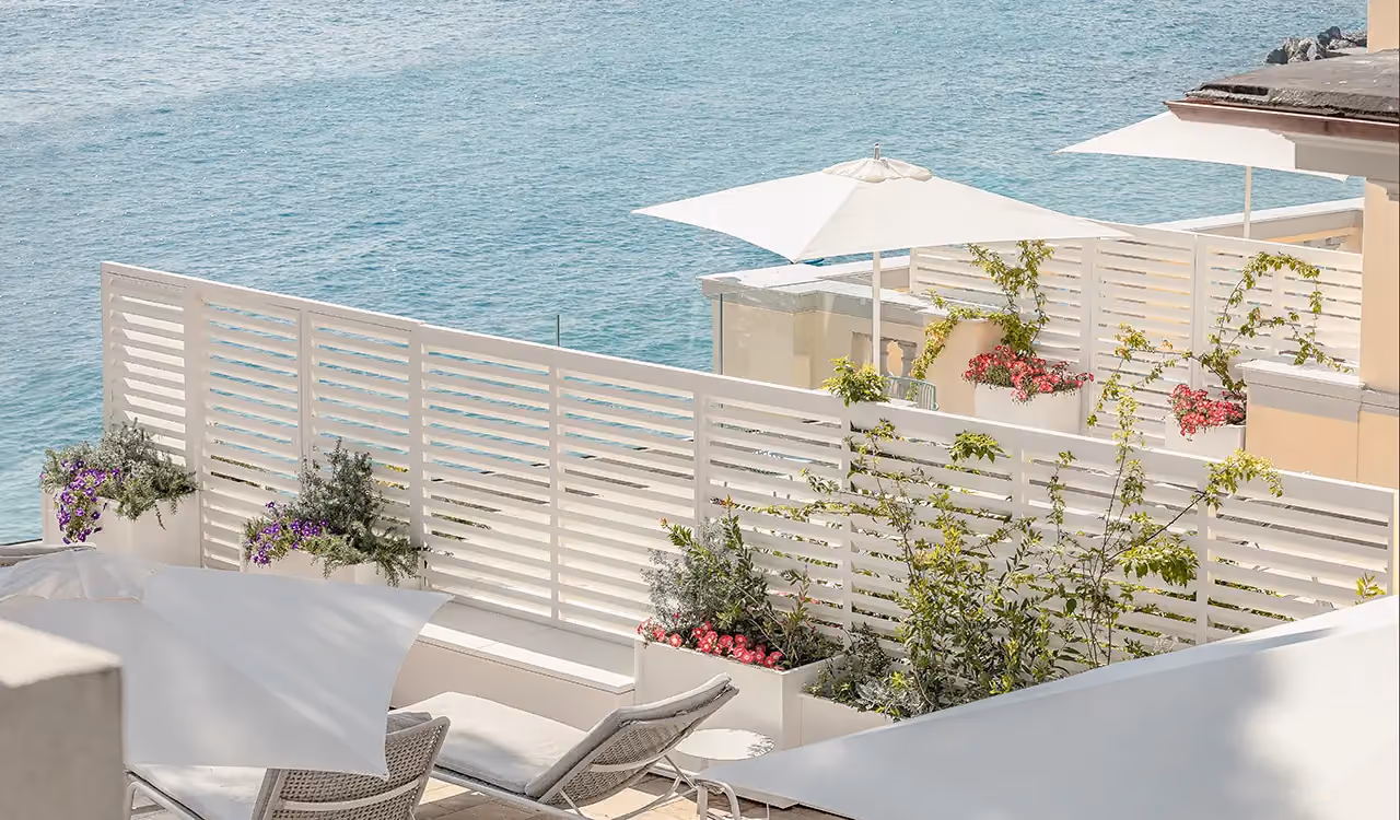 Terrazza sul mare con paraventi bianchi a listelli, lettini e fioriere fiorite
